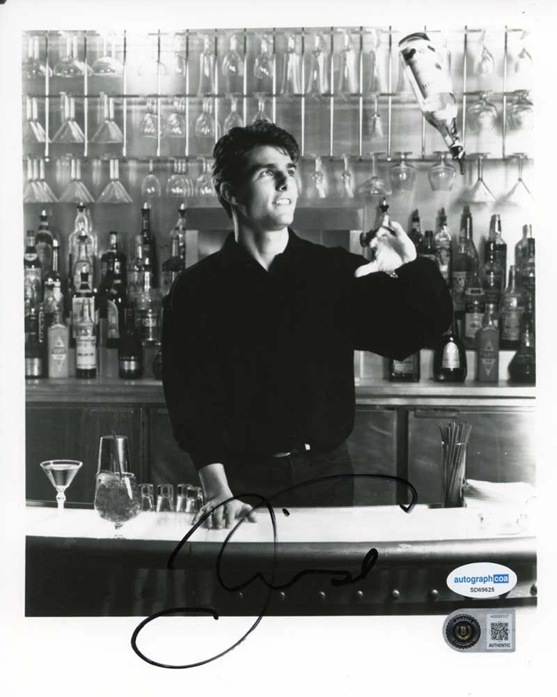 A black-and-white Cocktail still of Tom Cruise behind a bar tossing a bottle, signed across the bar top in black marker, with two small authentication stickers in the lower right corner.