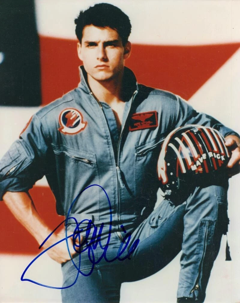 A colour Top Gun publicity photograph of Tom Cruise in a flight suit holding a Maverick helmet, signed in blue ink across his flight suit.